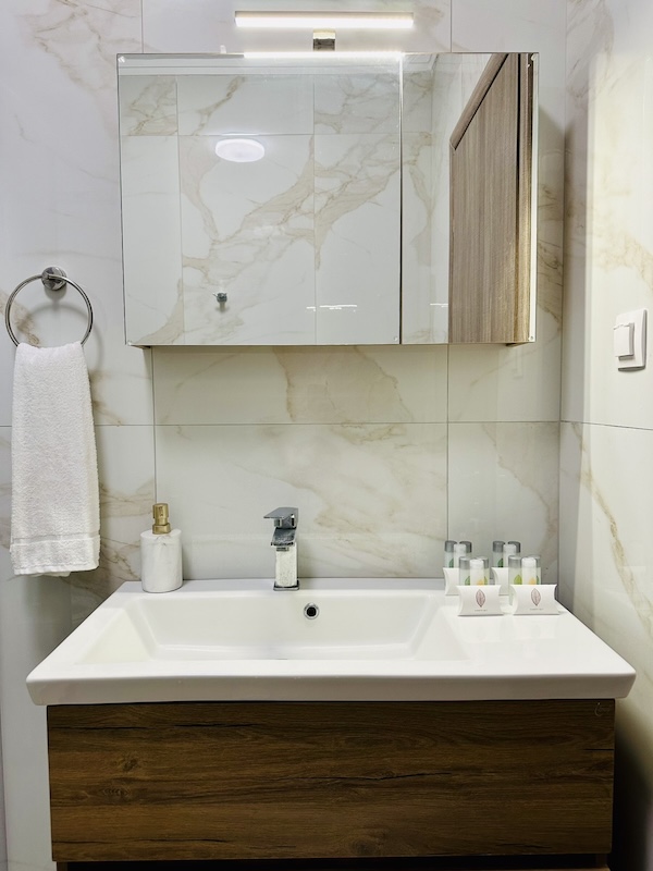 Bathroom washbasin with mirror cabinet and marble-effect tiles at Lora Family Apartment