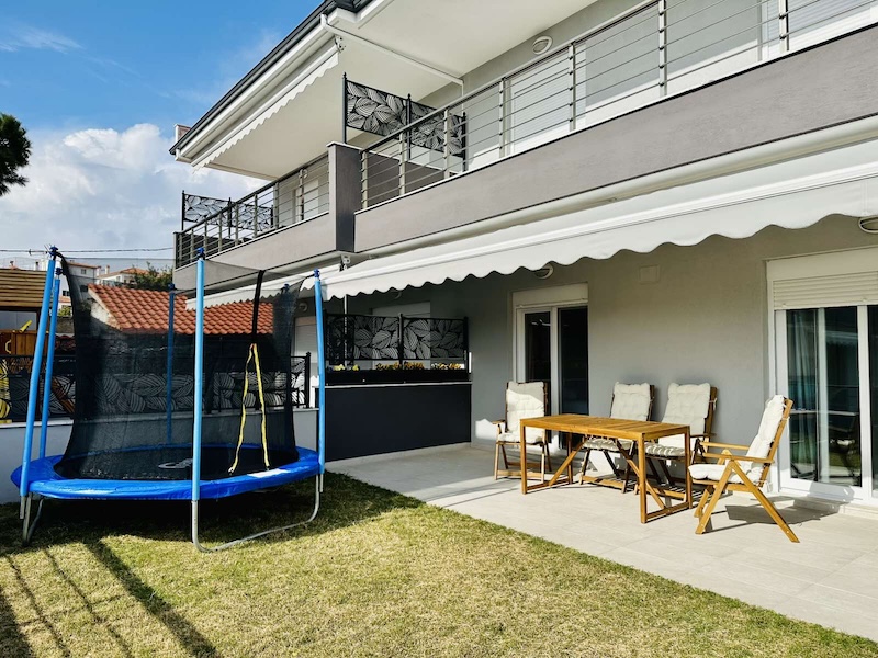 Patio with awning, outdoor dining table and the kids' trampoline on the lawn at Lora Family Apartment, Nikiti