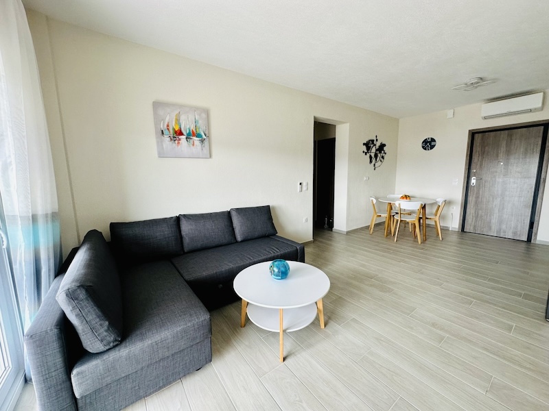 Open-plan living room with grey corner sofa, coffee table and dining table for four at Lora Family Apartment